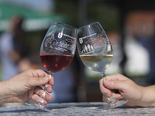 Foto: 2 Hände die ein Weinglas mit Rüsselheim-Motiv in der Hand halten