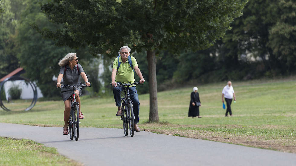 Eine Mann und eine Frau die am Mainvorland Fahrrad fahren. Im Hintergrund ein Mann und eine Frau die spazieren gehen.