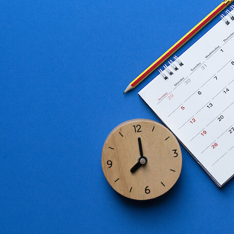 Ein Kalender, eine Uhr und ein Bleistift auf blauem Hintergrund.