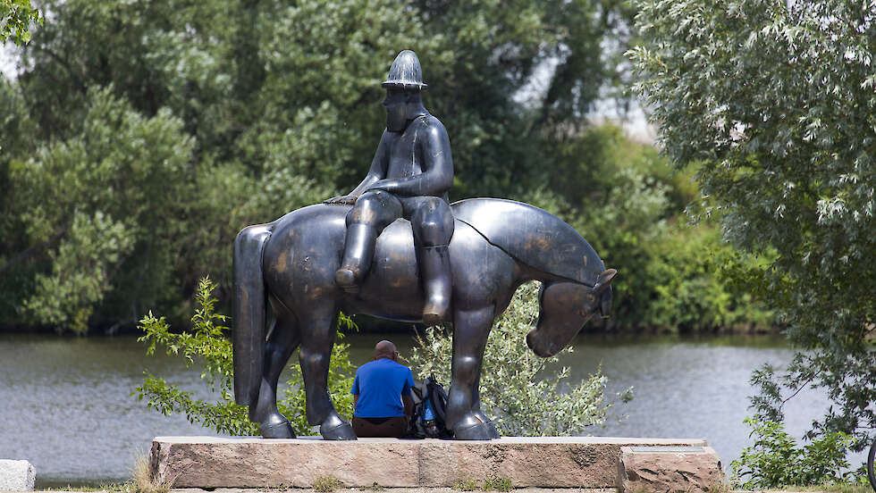 Leinreiter-Skulptur: Ein Mann der auf einem Pferd sitzt. Zwischen den Beinen der Skultur sitzt ein Besucher.