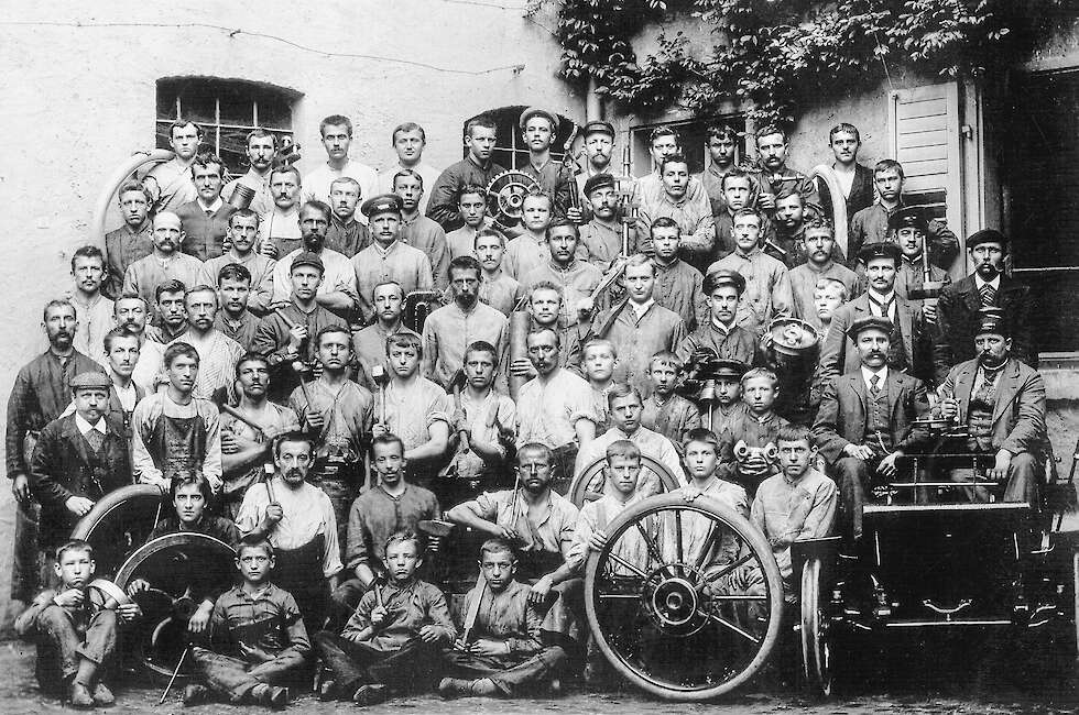 Dieses Foto ist ohne Farbe, weil es vor langer Zeit aufgenommen wurde. Auf dem Foto sieht man Männer, die vor vielen Jahren bei der Firma Opel gearbeitet haben.