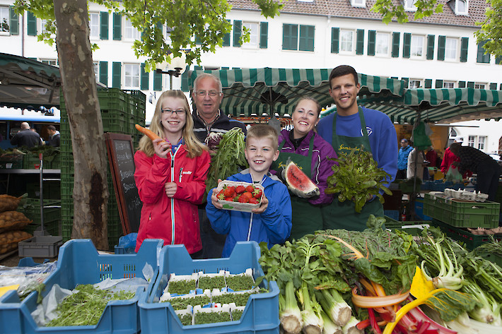 Marktstand mit verschiedenen Obst- und Gemüsesorten und Marktpersonal