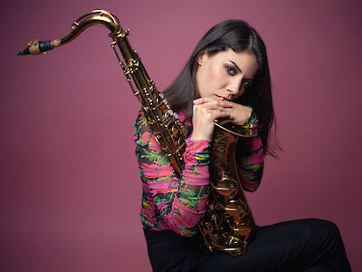 Melissa Aldana knieend, mit einem Saxophon auf dem Schoß.