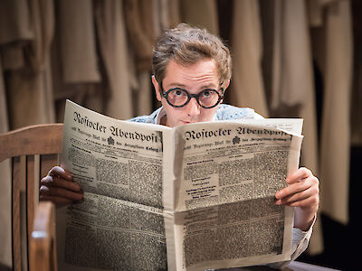 Ein Darsteller liest sitzend eine Zeitung