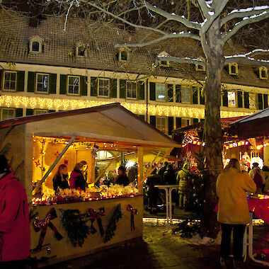 Beleuchtete Stände auf dem Weihnachtsmarkt am Abend mit Besucherinnen und Besuchern.