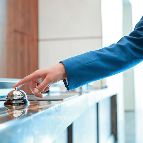 Eine Hand drückt auf eine Klingel an einer Hotelrezeption