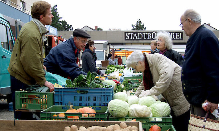 Marktstand mit verschiedenen Gemüsesorten, Kunden und Marktpersonal