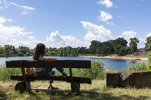 Eine Frau sitzt auf einer Bank am Waldschwimmbad