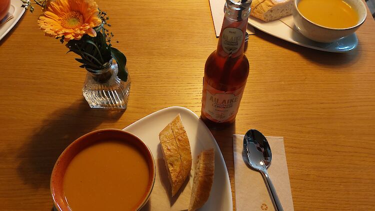 Ein Teller Kürbissuppe und 2 Stückchen Weißbrot, angerichtet auf einem Tisch.