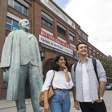 Ein junges Paar steht neben der Adam-Opel-Statue vor dem Opel-Altwerk